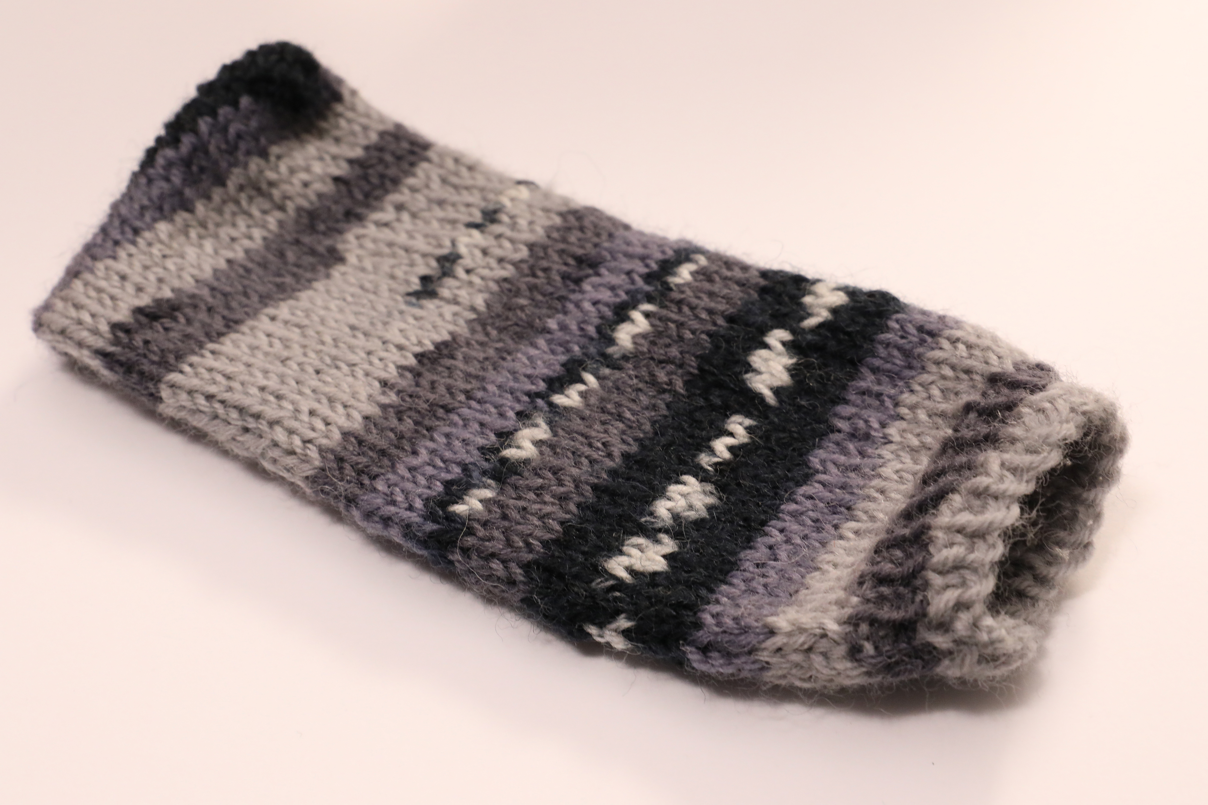 A knit, monochrome (black, white, and shades of grey) cellphone cozy on a white background. There is no cellphone present.