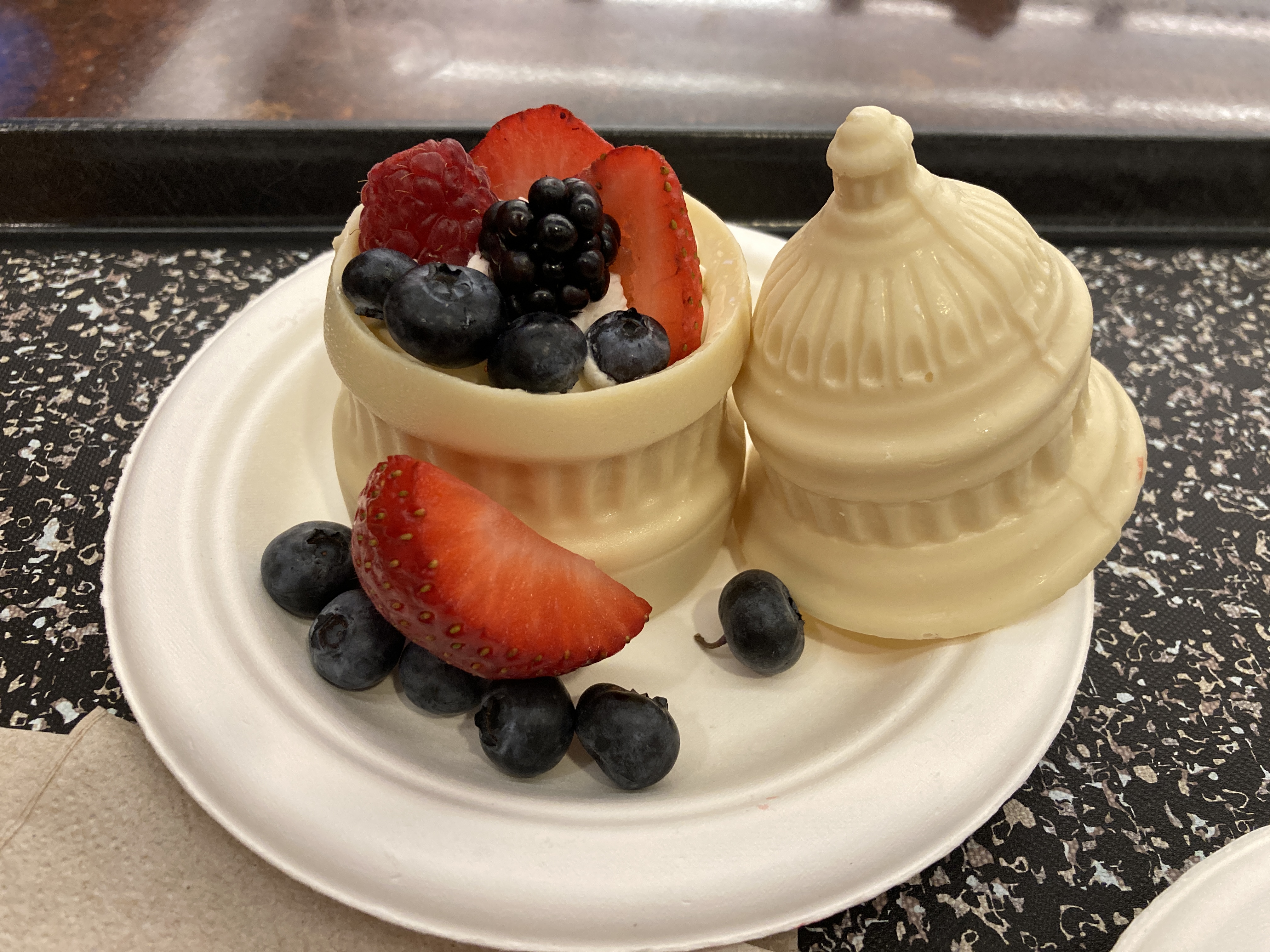 A picture of a white chocolate dessert formed in the shape of the US Capitol building's dome, filled with strawberries, blueberries, and whipped cream.